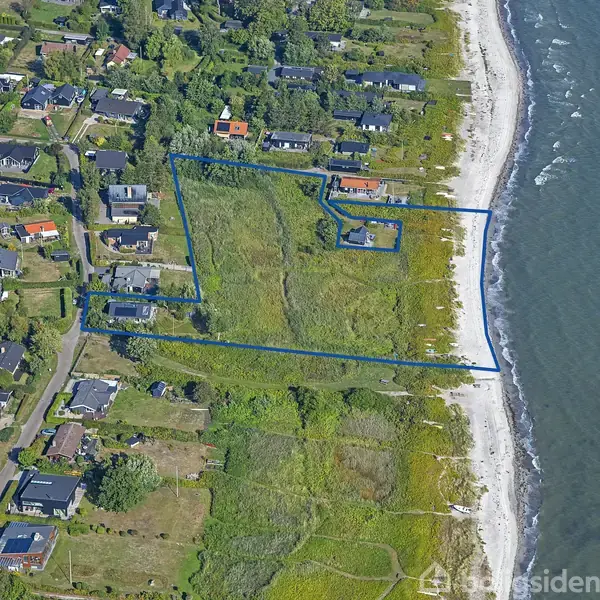 En række huse ligger tæt ved kysten, omgivet af grønne marker. Et blåt omrids markerer et område ved stranden, hvor havet møder kystlinjen.