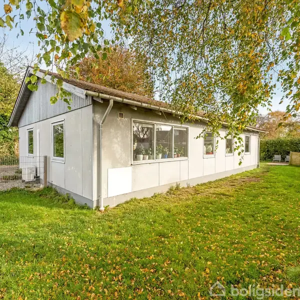 Huset er hvidt og enkelt med mange vinduer, som spejler omgivelserne. Det står på en velholdt grøn græsplæne, omkranset af træer og en lille grussti.