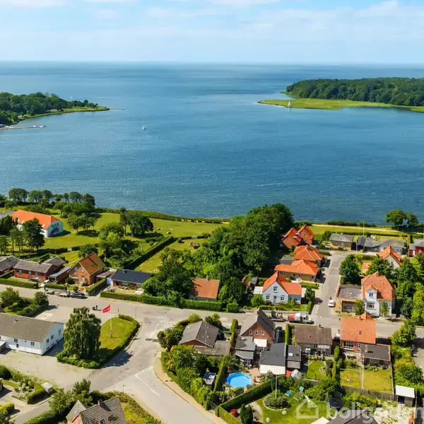 Kystby set fra luften viser række af huse med røde tage langs en kystlinje. Havet i baggrunden skaber en rolig, naturskøn atmosfære.