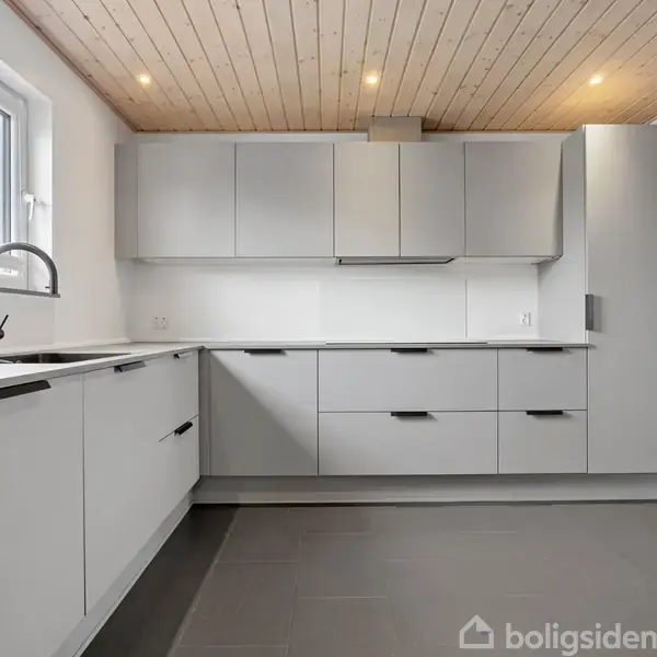 Køkken med grå skabe og skuffer, moderne vandhane ved et vindue. Lyst loft med spotlys. Rummet ser rummeligt og velorganiseret ud.