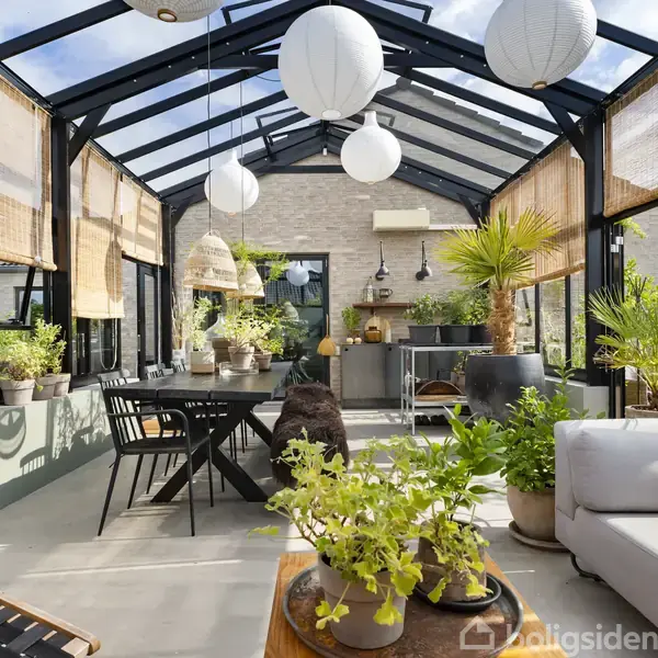 Vinteropvarmet udestue med glasvægge og loft. Rattanmøbler, bord med stole, hængende pærer og mange grønne planter skaber en hyggelig atmosfære. Rolige omgivelser med udsigt til grønt område.