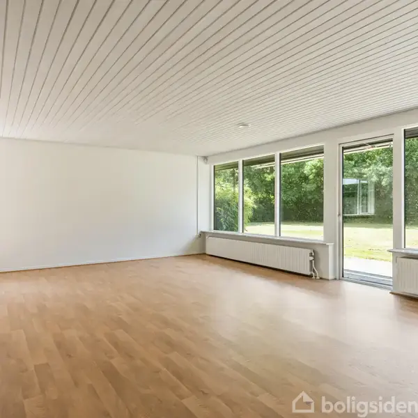 Et hvidt murstenshus med sort tag ligger ved en vej. Huset har en garage og er omgivet af grønne hække og træer.