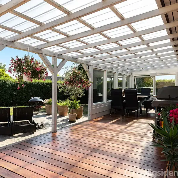 En overdækket terrasse med trædæk har siddemøbler og blomsterkrukker. Omkring terrassen er en have med hække. Terrasse taget er lavet af gennemsigtige paneler, der lader lys komme igennem.