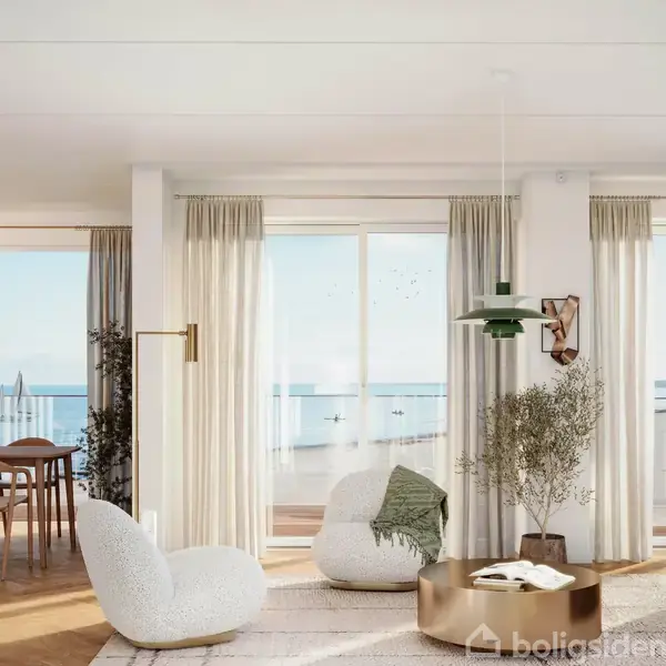 Et moderne, lyst stueområde med hvide møbler foran store vinduer, der giver udsigt til havet. Ved siden af er et spisebord med stole. Sollys strømmer ind, skaber en lys atmosfære.