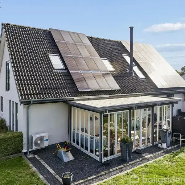 Et moderne hus med solpaneler på taget. Foran huset er der en stor udestue omgivet af en velplejet have. Vejrstationer og haveredskaber er placeret udenfor.