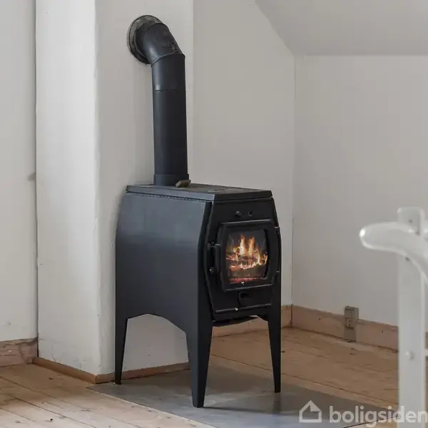 En sort brændeovn står solidt i hjørnet af et rum, med flammer synlige bag glasdøren. Omgivet af hvide vægge og et trægulv, nær en radiator.