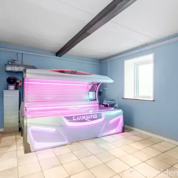 Solarium ligger i et rum med lyseblå vægge og lysebrune fliser. Det automatiske solarieapparat er oplyst med pink lys og har mærket "Luxura". Vinduet bringer naturligt lys ind.
