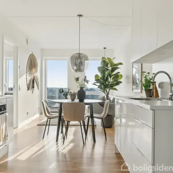 Lyst køkken med spisebord centralt, omkranset af fem stole. Køkkenskabe og bordplader med planter og køkkenredskaber. Store vinduer giver udsigt til en klar himmel.