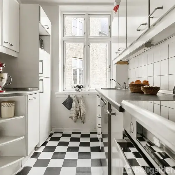 Rødt køkkenapparat står på bordet, omgivet af hvide skabe i køkken med sort-hvidt skakternet gulv. En hvidtopvask og vindue i baggrunden med et lysskær ind i rummet.