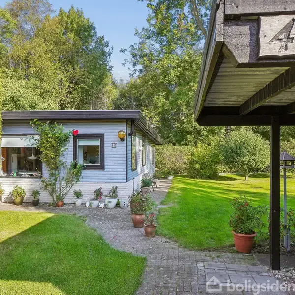 Et hus med blå ydervægge har blomster i potter foran. En græsplæne og træer omgiver huset. Husnummeret "4" ses på et tagudhæng.