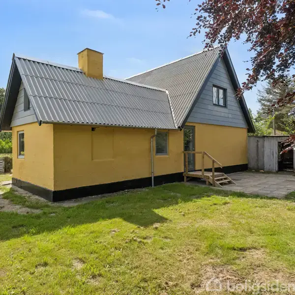 Hus med gult ydre står i en solrig have. Triste trapper fører til indgangen. Omkring huset er der græsplæne og træer, der skaber en stille atmosfære.