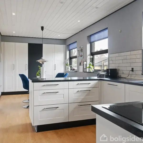 En sø er omringet af græs og buske, med en enkelt gadelampe til venstre i billedet og en moderne bygning til højre.