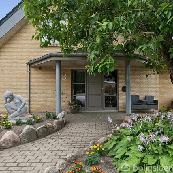 Hus med gul murstensfacade og gråt tag. En statue i tænksom position står ved siden af indgangen. En havegang omgivet af blomster og en stor busk fører til døren. Nummer 31 er synligt på væggen.