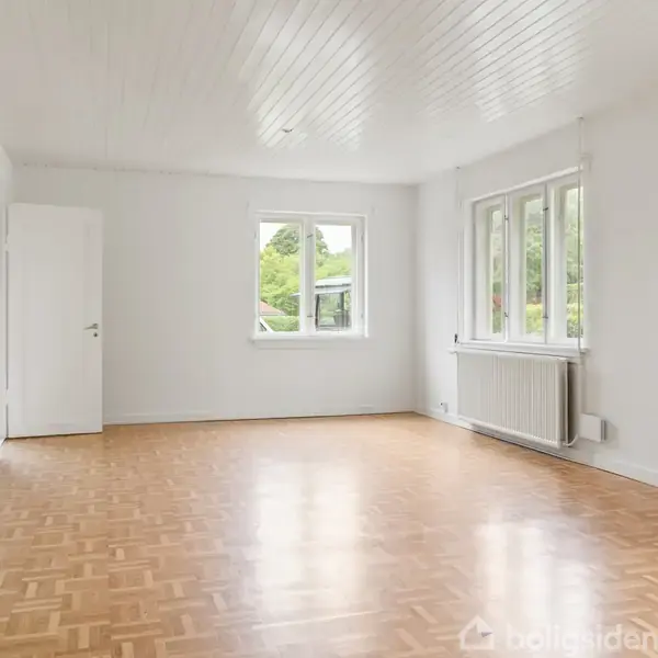 Et lyst, tomt rum med parketgulv og hvidmalede vægge. En radiator under store vinduer giver udsigt til en grøn have. En dør står åben til venstre.