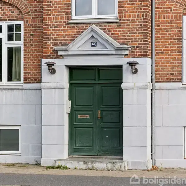 Grøn hoveddør står stille i en murstensbygning med hvide vinduesrammer og grå sokkel. Over døren er der skrevet "54". To lamper flankerer døren i en bymæssig gade.