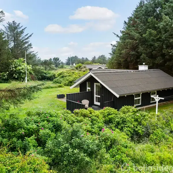 Et sort træhus står stille omgivet af frodig grøn vegetation i en skovklædt have i fredfyldt natur.
