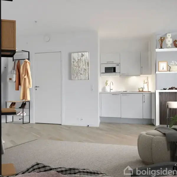 Et moderne køkken- og stueområde med hvide skabe, en mikroovn og en vask. Rummet er lyst indrettet med planter og dekorationer. En åben reol adskiller soveområdet fra køkkenet.