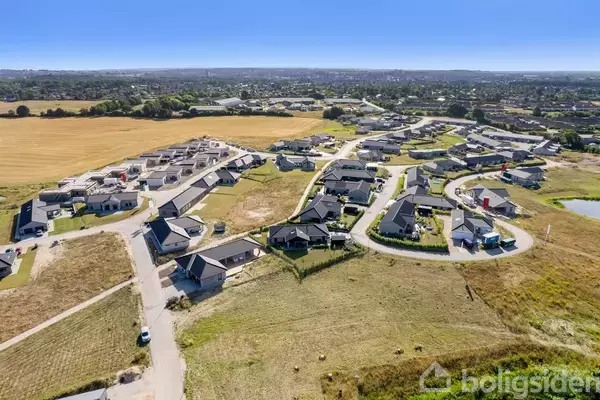 Bebyggelse med en række huse placeret langs snoede veje, omgivet af åbne marker og en by i baggrunden.vej.