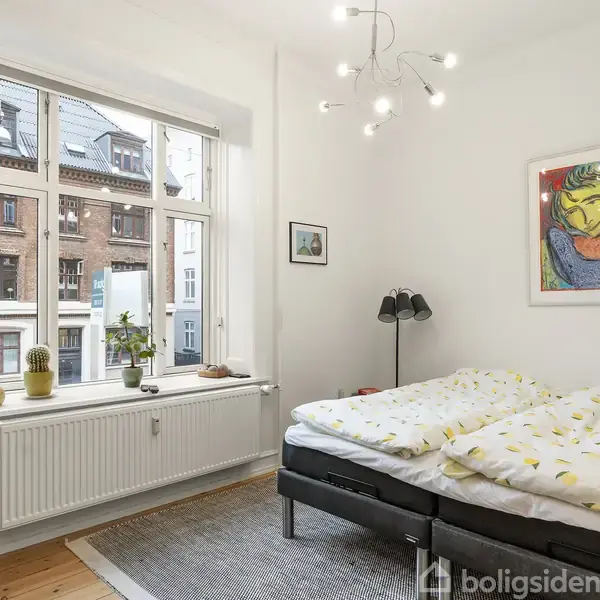 Spisebord med grøn dug, omgivet af otte stole, står midt i et lyst rum med hvide vægge. Blomsterdekorationer pryder bordet, mens store vinduer og planter skaber en hyggelig atmosfære.