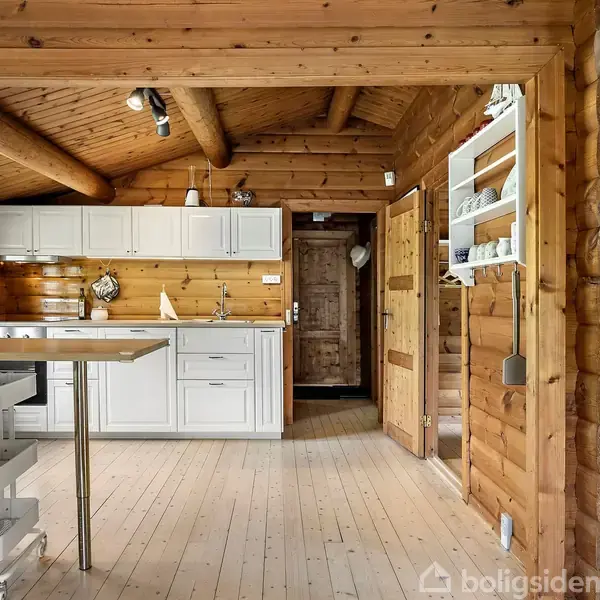 Et lyst træinteriør af en hytte med et køkken, der har hvide skabe og en køkkenø. Til højre hænger et skilt med teksten: "LIFE AT THE END OF THE ZONE."