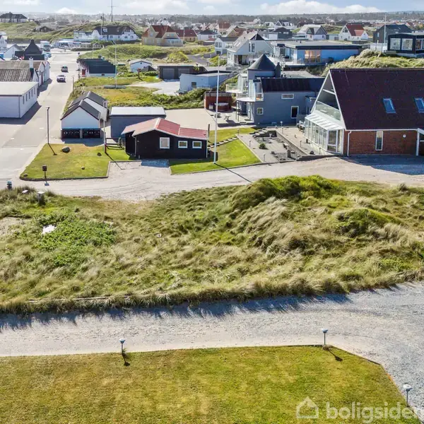 Græsbevokset bakke ligger stille i en lille by med huse omkring. Asfalteret vej og stier ses på begge sider af bakken.