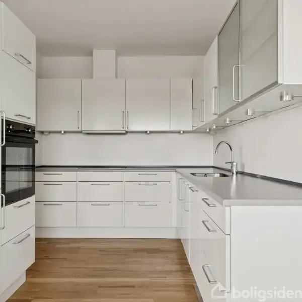 Et moderne køkken med hvide skabe og sorte bordplader. Skabene er monteret over og under en indbygget ovn. En hvid vask er placeret i bordpladen. Trægulve udgør gulvet.