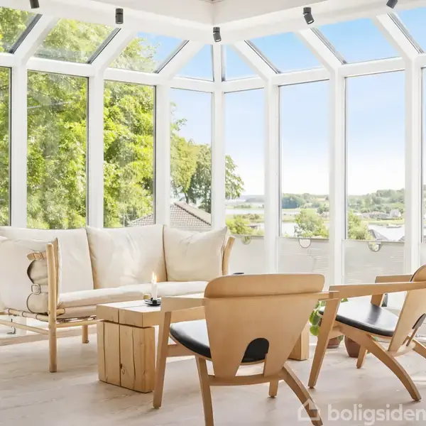 En lys stue med glasvægge, hvor en beige sofa og to træstole omringer et lyst træbord med blomster. Der er grønne træer udenfor, skaber en hyggelig atmosfære.