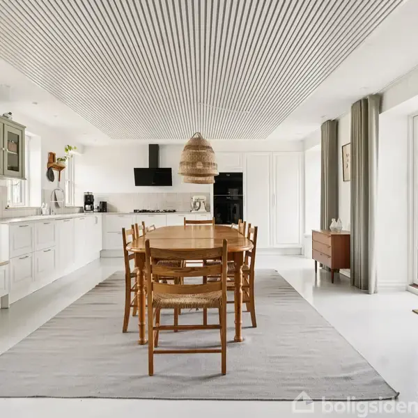 Et træbord omgivet af seks stole står på et gråt tæppe i et lyst køkken-alrum med hvide skabe, en hængende lampe, og en stor glasdør der fører ud til en have.