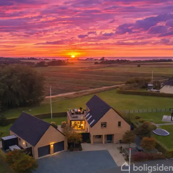 To huse står stille i en landlig have under en dramatisk, farverig solnedgang. Huse omgives af store grønne marker og træer. Tekst: "Visualisering".