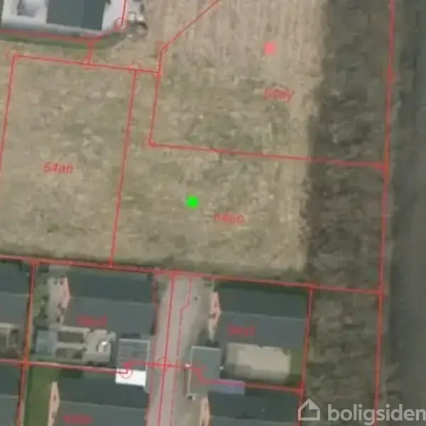 Luftfoto viser boligområde med matrikelopdelinger, markeret med røde linjer og numre som 558a og 563, omgivet af bygninger til venstre og åbent land til højre.