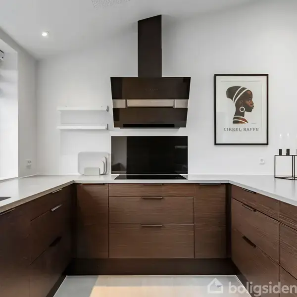 Køkken med mørke træskabe står i U-form, omfavner en indbygget ovn med sort emhætte. Vinduet har persienner og planter. Plakat siger "CIRELL KAFFE" med afbilledet profil.