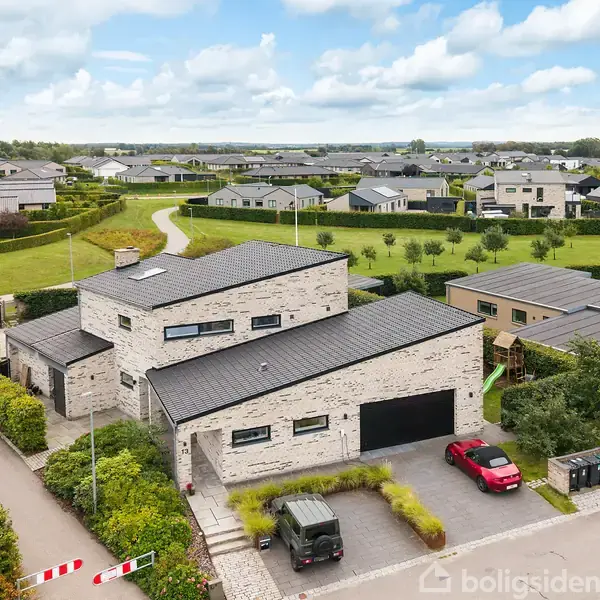 En moderne villa står udenfor med et fladt tag og store vinduer. Den er omgivet af en have, og en rød bil er parkeret foran. Baggrunden viser et parcelhuskvarter.