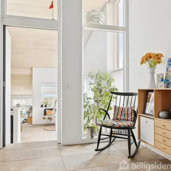 Sort stol med farverig pude står ved siden af et skab med blomster på. Lyse rum med grønne planter oplyst af naturligt lys.