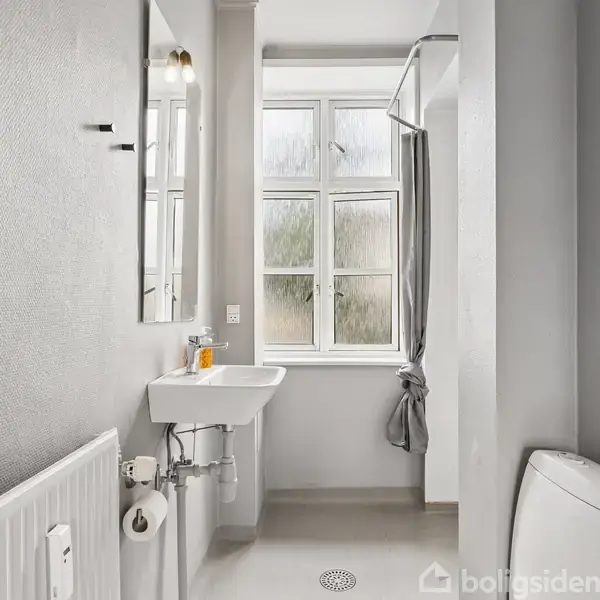 Håndvask og toilet i et lyst badeværelse, med et stort vindue i baggrunden og en grå bruseforhæng ved siden af. En radiator er placeret til venstre.