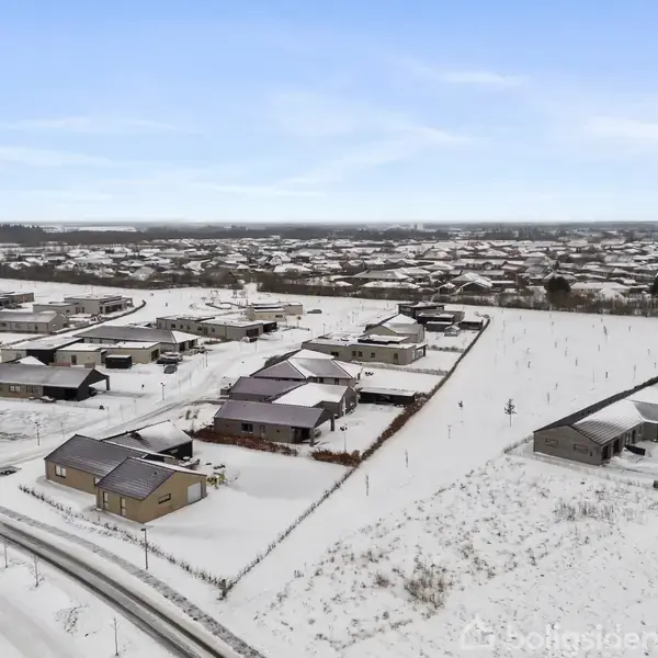 Boliger belagt med sne står stille i et roligt boligkvarter. Vejene er dækket af sne, og området strækker sig mod horisonten med flere huse og åbne marker.