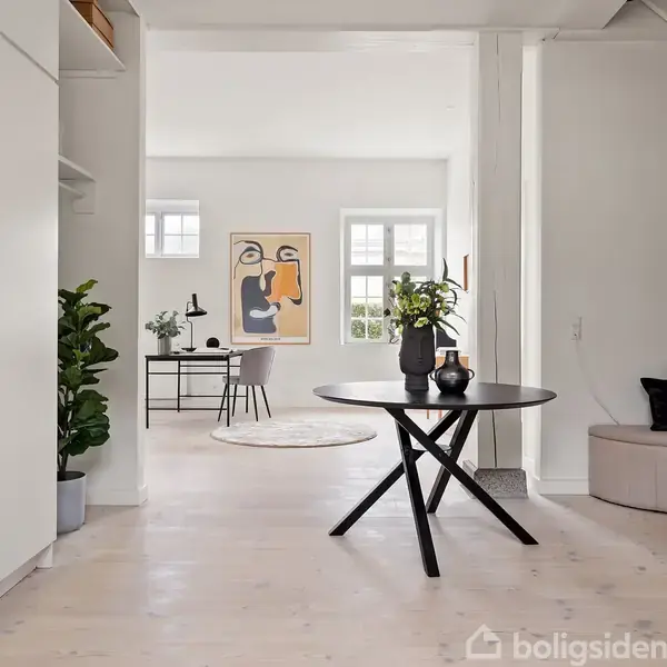 En rund bordplade er dekoreret med planter; den står i forgrunden. Bagved ses et arbejdsområde med et skrivebord og stol. Rummet er lyst med kunst på væggen.