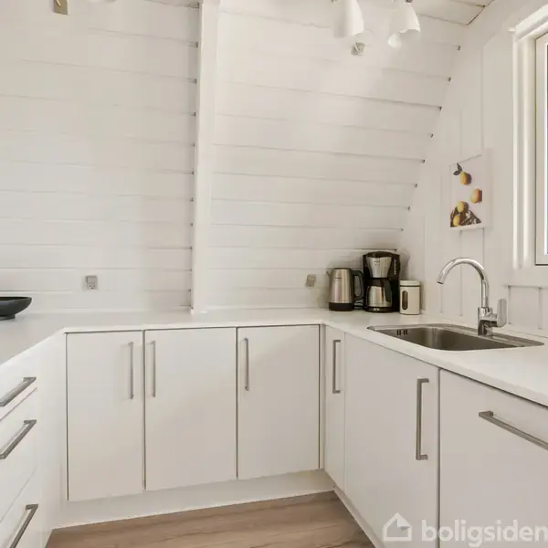 En stue har en grå hjørnesofa og rundt spisebord med sorte stole. Store vinduer bagved åbner ud mod en terrasse. Tv'en hænger på væggen, og rummet er lyst og moderne.