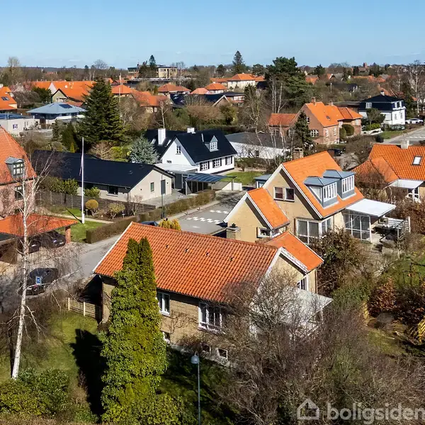 Række af huse med røde tegltage strækker sig gennem en forstad. Træer og haver omgiver boligerne, hvilket skaber en fredfyldt atmosfære.