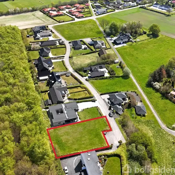 Grønt bælte markerer en ubebygget grund tæt ved boligområde. Omgivet af skov til venstre og flere huse og veje til højre.