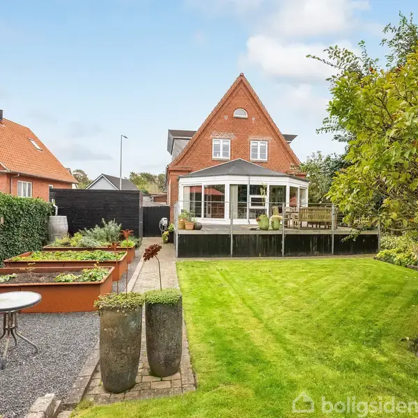 Hus i mursten med gavl, bagtil med stor veranda. Handlingsløst. Omgivet af en velholdt græsplæne, blomsterbede og siddeplads.