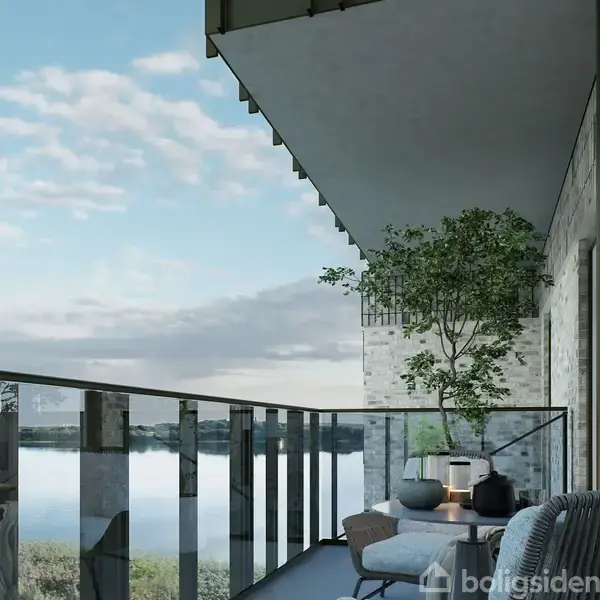 Balkon med sofa og potteplanter, indrettet til afslapning, med udsigt over en stille sø i baggrunden. Skyer og blå himmel fuldender den fredelige stemning.