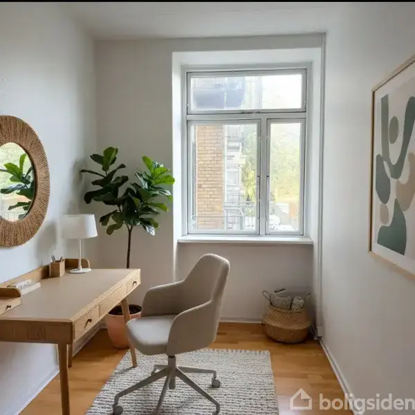 Et skrivebord med lampe og kontorstol står ved et vindue. En plante og et rundt spejl hænger på væggen. Der er også et lille tæppe og vægdekoration.