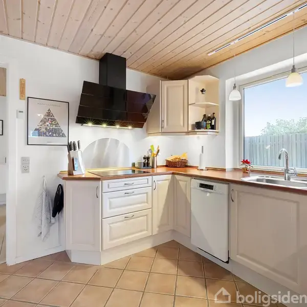 Køkken med hvidt interiør, træloft og klinkegulv. Kogeplade og emhætte er centreret. Et vindue og vask til højre. Lysindfald fra vinduet. Ingen synlig tekst.