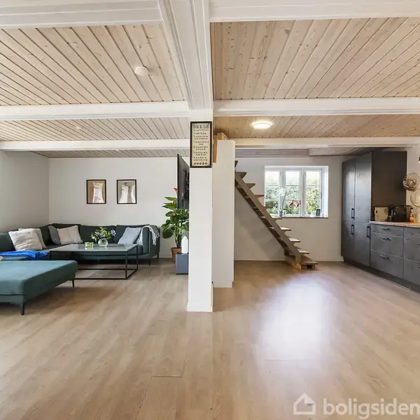 Stue med trægulv og loft, en hjørnesofa til venstre, tæppe og billeder på væggen. Højre side har et moderne køkken med skab og bordplade. Tekst på skilt: "A long time ago, in a galaxy far, far away..."