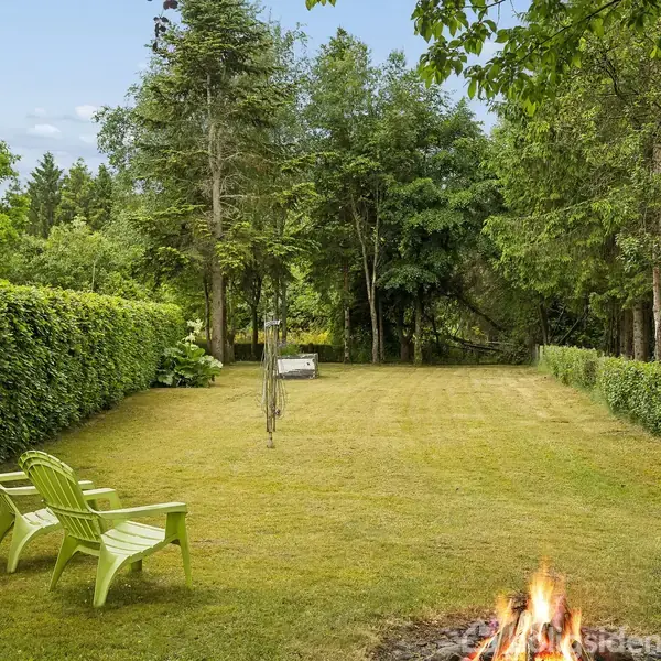 Køkken med hvidt interiør har en rund spisebord med fire stole. I baggrunden er der komfur, ovn og køleskab. Rummet har træloft og trappe til venstre.
