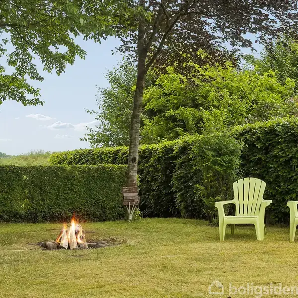 Et lyst gangområde med planter og et tæppe. Til venstre hænger et maleri og en radiator er synlig. En lille bænk står for enden med en pude med teksten "THERE IS NO PLACE LIKE HOME". Til højre er en trappe opad.