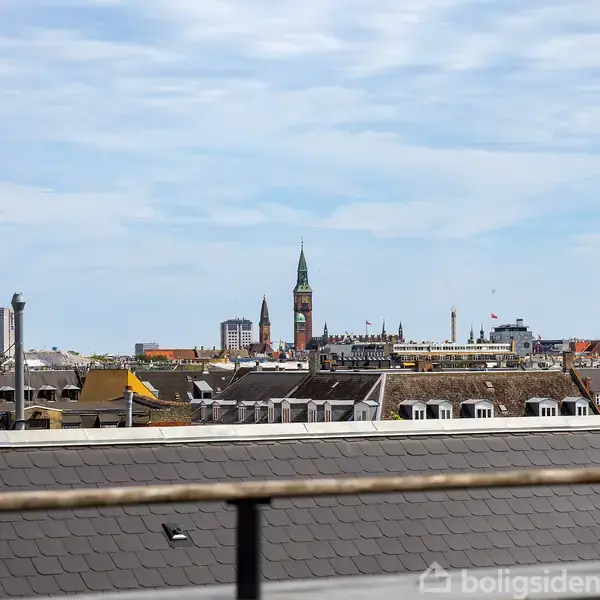 Byens skyline med tårne rager op over hustagene, under en blå himmel med spredte skyer.