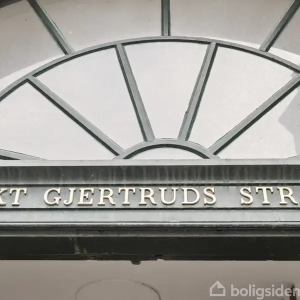 En metalskilt viser teksten "SANKT GJERTRUDS STRÆDE" i blokbogstaver placeret over en halvcirkelformet vindue med sprosser.