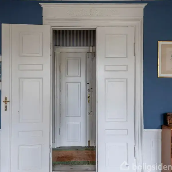 Døre åbner ind til en hvid hoveddør med paneldesign, omkranset af blå vægge og en gylden ramme til højre.