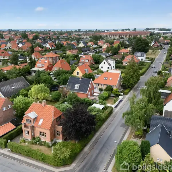 Boligkvarter med rødtage huse i et beboelsesområde. Husene er omgivet af haver og grønne træer. Adskillige veje løber gennem landskabet, og man kan se bygningskomplekser i baggrunden.